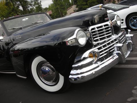 1998 Ford Crown Victoria - A classic black convertible with prominent chrome accents is parked next to a white car.