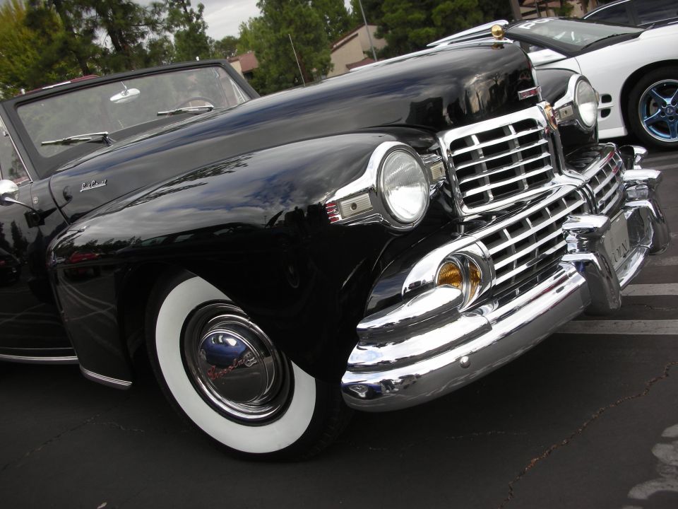 Black convertible with whitewall tires and chrome grille, viewed from the front quarter