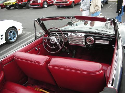 1998 Ford Crown Victoria - The interior of a vintage convertible with red upholstery is visible, with other vehicles parked behind.