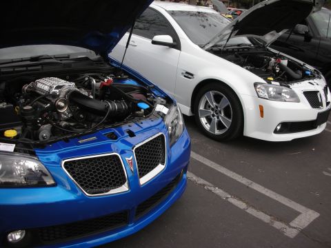 1998 Ford Crown Victoria - Two Pontiac G8s are parked side-by-side with their hoods open, revealing their engines.