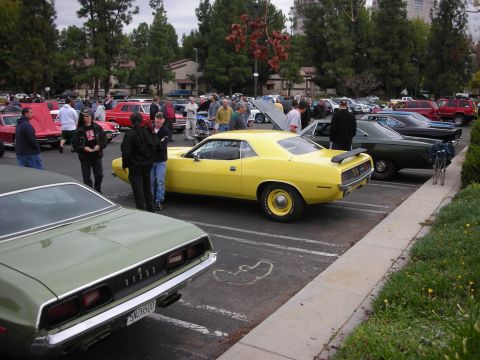 1998 Ford Crown Victoria - A car show features several classic American muscle cars, including a yellow Plymouth Barracuda and a green Dodge Challenger.