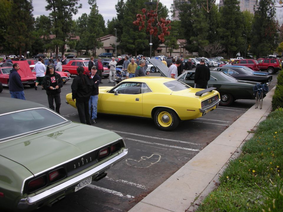 Yellow Plymouth Barracuda and green Dodge Challenger parked at a car show with people around