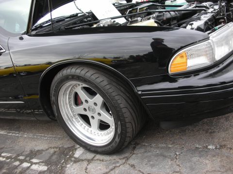 1998 Ford Crown Victoria - The front quarter panel and wheel of a black sedan are visible, with the hood open to show the engine compartment.