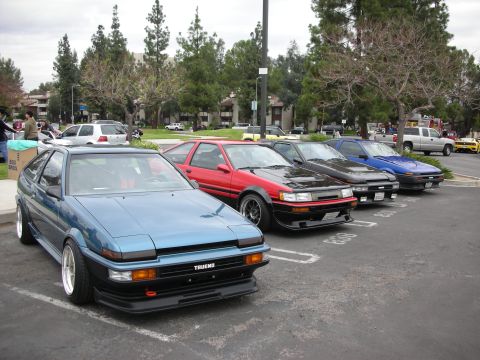 1998 Ford Crown Victoria - Several Toyota AE86 coupes are parked in a lot, with a blue one in the foreground.