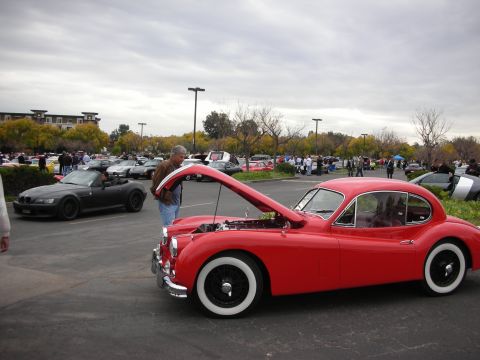 1998 Ford Crown Victoria - A man inspects the engine of a classic red coupe at a car show with other vehicles in the background.
