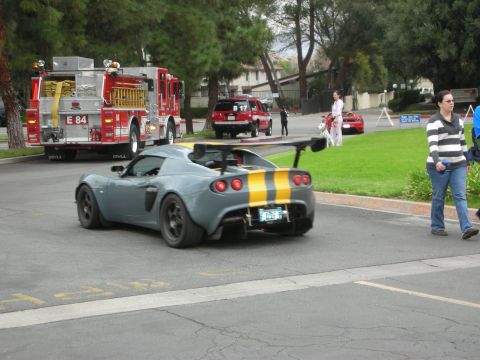 1998 Ford Crown Victoria - A Lotus Elise with racing stripes and a large rear spoiler is seen driving past emergency vehicles and other cars.