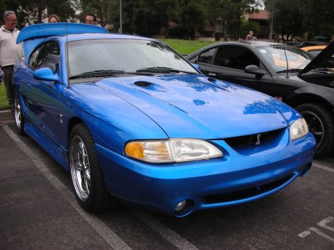 1998 Ford Crown Victoria - Blue Ford Mustang Cobra from the mid-90s, a prominent rear spoiler and hood scoops.