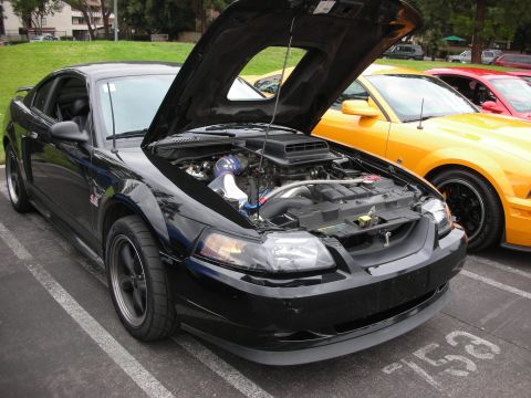 1998 Ford Crown Victoria - A black Ford Mustang is parked with its hood open, revealing the engine, next to a yellow Mustang.
