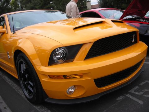 1998 Ford Crown Victoria - A bright orange Ford Mustang Shelby GT500 is parked next to another car with its hood up.