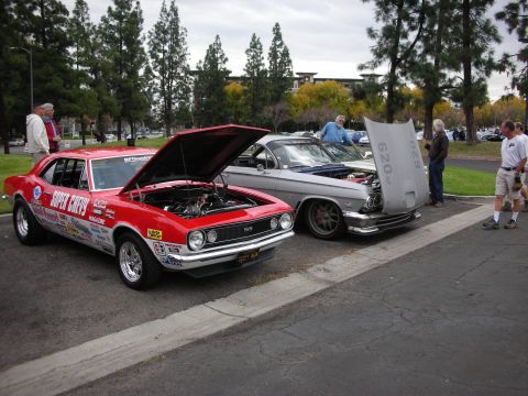 1998 Ford Crown Victoria - A red 1967 Chevrolet Camaro SS is parked next to a silver car, both with hoods open, at an outdoor event.