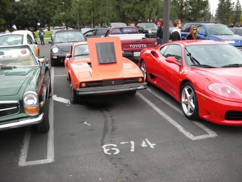 1998 Ford Crown Victoria - Several cars are parked in a lot, including an orange sports car with its hood raised.