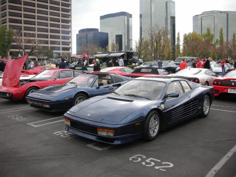 1998 Ford Crown Victoria - A blue Ferrari Testarossa is parked in a lot alongside other vehicles, with modern buildings visible in the background.