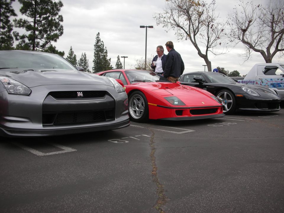 Several sports cars including a red Ferrari, a gray Nissan GT-R, and a black Chevrolet Corvette parked in a lot