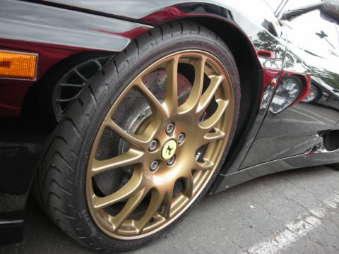 1998 Ford Crown Victoria - Close-up of a gold Ferrari wheel and tire on a black car, showing reflections of other vehicles in the polished bodywork.