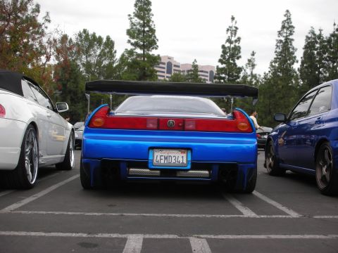 1998 Ford Crown Victoria - A modified blue sports car is parked in a lot, a prominent rear spoiler and custom exhaust tips.
