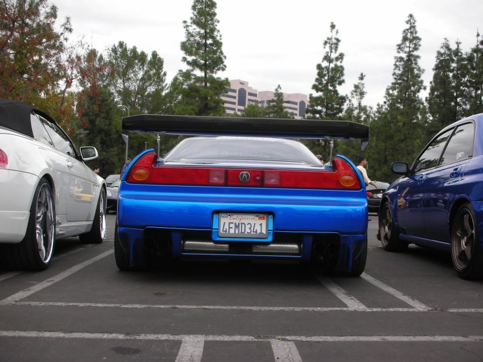 Blue sports car with a big wing and custom exhaust parked next to a white convertible and a blue sedan