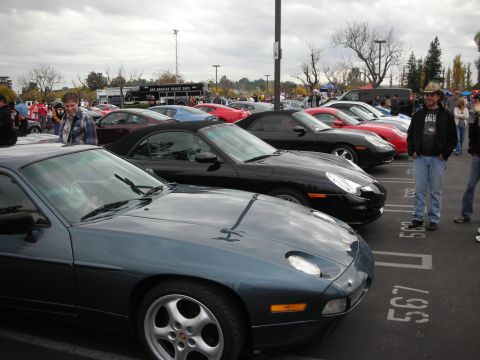 1998 Ford Crown Victoria - A line of cars are parked in a lot, with a dark blue Porsche 928 in the foreground.
