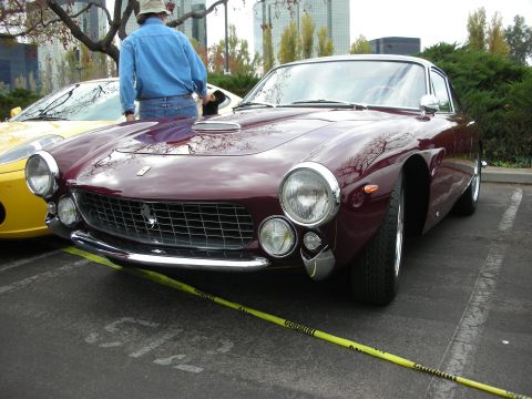 1998 Ford Crown Victoria - A classic maroon Ferrari is parked in a lot next to a yellow sports car, with a person standing nearby.