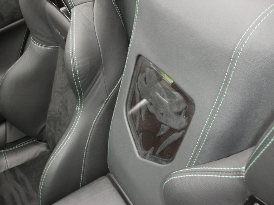 Car interior showing black leather seats with green stitching and a clear plastic insert with a snake logo