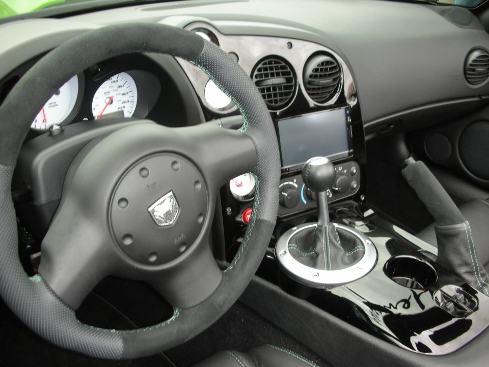 Car interior with a steering wheel, dashboard, gear shift, and cup holders. The steering wheel has a snake emblem