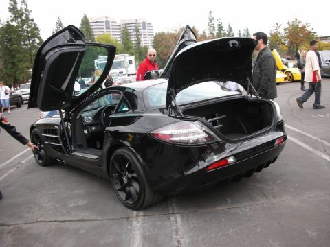 1998 Ford Crown Victoria - Black sports car with gullwing doors and open trunk, parked at an outdoor event with other vehicles present.