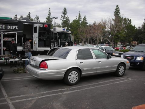 1998 Ford Crown Victoria - A silver sedan is parked in a lot next to a police department truck and other vehicles.