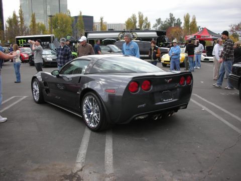 1998 Ford Crown Victoria - A dark gray Chevrolet Corvette is parked at an outdoor event with several people around.