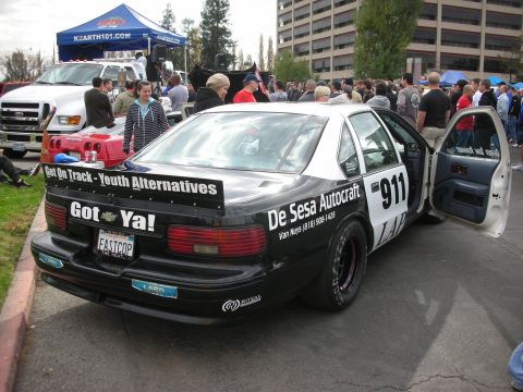 1998 Ford Crown Victoria - This modified police car features racing slicks and a prominent spoiler, with custom decals and a license plate reading 'FASTCOP'.