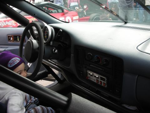 1998 Ford Crown Victoria - The interior of a modified vehicle shows a roll cage and racing gauges, with a child observing the scene.
