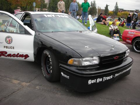 1998 Ford Crown Victoria - A modified police car with racing tires and graphics is parked at an outdoor event.