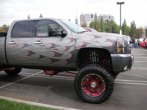1998 Ford Crown Victoria - A customized pickup truck with flame graphics and large off-road tires is parked in a lot.