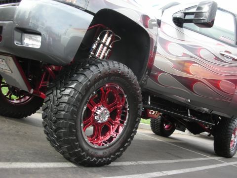 1998 Ford Crown Victoria - A heavily modified truck with custom flame paint and bright red wheels is shown from a low angle, highlighting its lifted suspension.