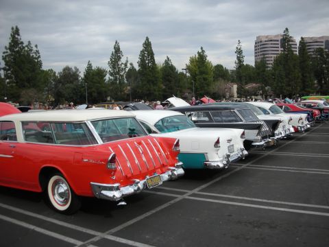 1998 Ford Crown Victoria - Several vintage cars are parked in a lot under a cloudy sky, with buildings in the background.