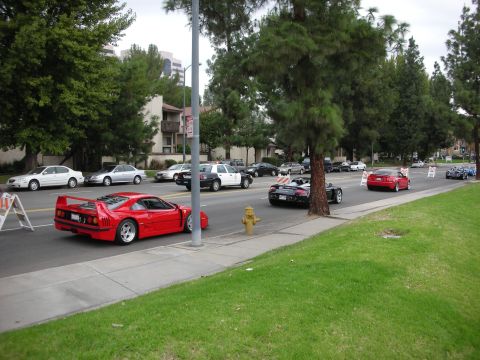 1998 Ford Crown Victoria - Multiple vehicles, including a red sports car and a police car, drive down a suburban street.
