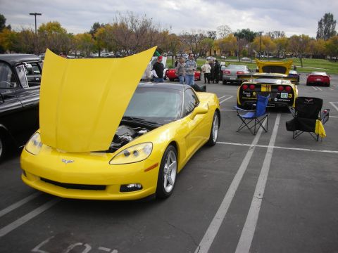 1998 Ford Crown Victoria - Photograph of a yellow Chevrolet Corvette with its hood raised at an outdoor car show.