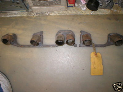 1953 Ford Mainline - A set of exhaust manifolds, likely for a V8 engine, is laid out on a concrete floor. The manifolds are made of cast metal and feature multi…