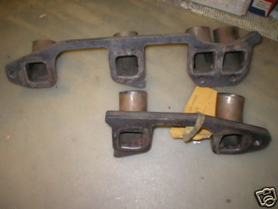 1953 Ford Mainline - A pair of cast-iron exhaust manifolds laid on newspaper, showing the rectangular head-flange ports and round copper-colored exhaust outlets.