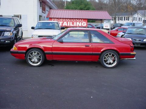 1990 Ford Mustang - A red 1990 Ford Mustang coupe is parked on asphalt in front of a building with a red awning that reads "PROFESSIONAL TAILING". Other vehicl…