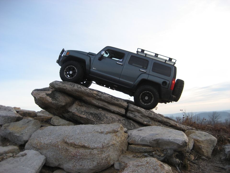 Dark gray SUV climbing over large rocks on a trail.