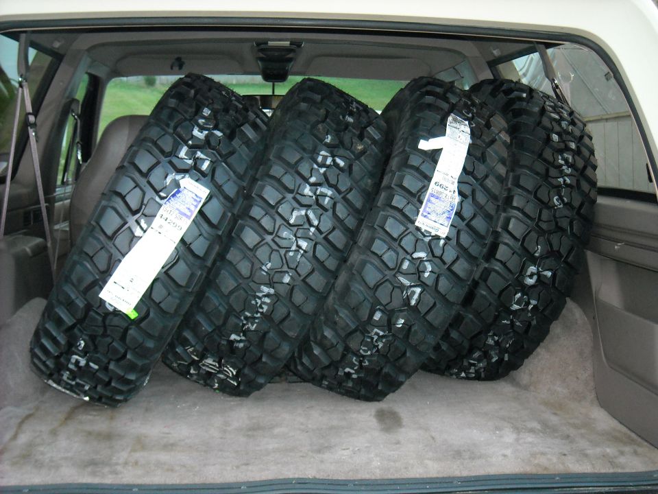 Four mud-terrain tires loaded in the cargo area of an SUV