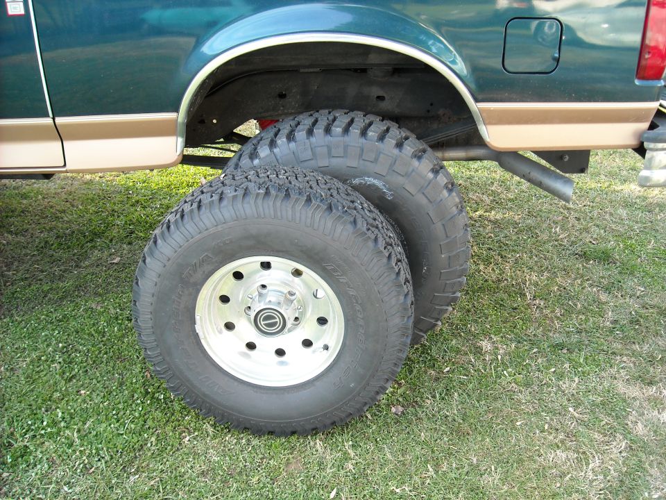 Two off-road tires on alloy wheels leaning against a lifted truck