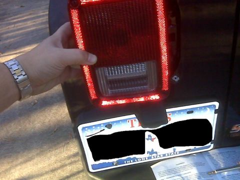 2008 Jeep Wrangler - A person's hand is holding a red LED taillight assembly over a Texas license plate on the rear of a dark-colored vehicle.
