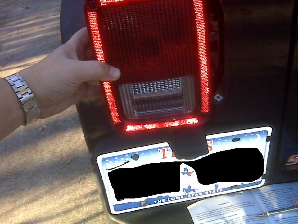 Hand holding red LED taillight over Texas license plate on vehicle rear.