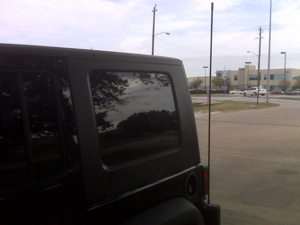 Black Jeep Wrangler rear passenger side, reflection of trees and clouds in window.