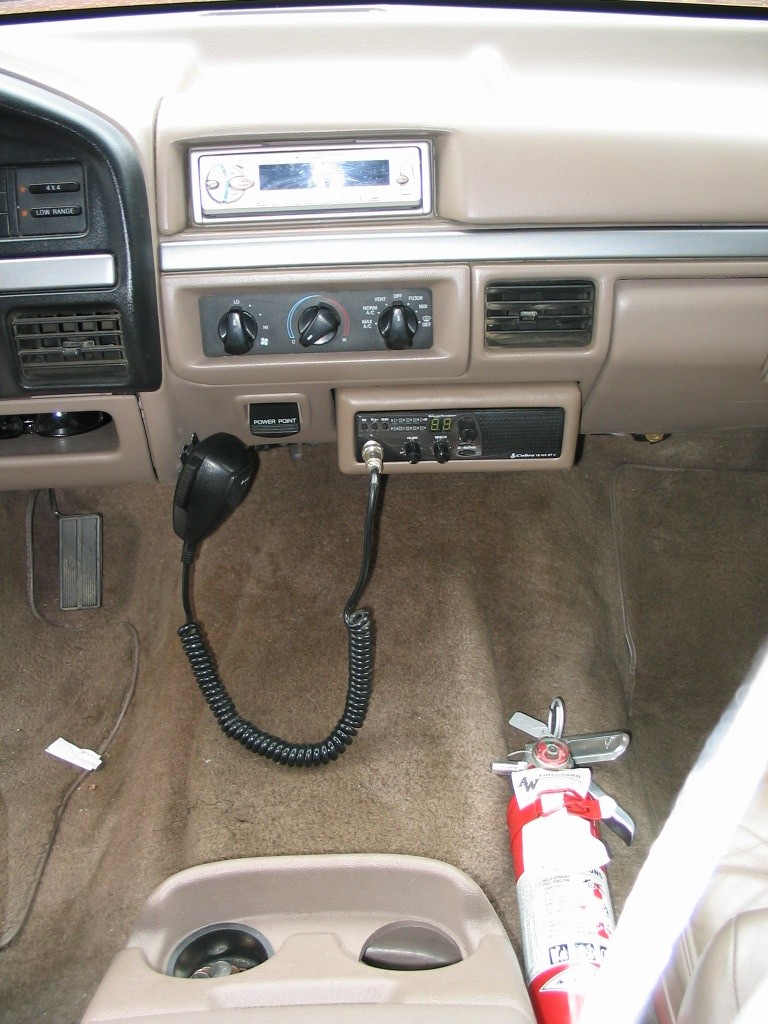Tan dash of a 1995 Bronco with aftermarket stereo, Cobra CB radio with coiled mic, and fire extinguisher on floor
