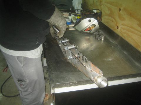 1990 Ford Bronco - Photo of a person fabricating a welded metal suspension link on a shop bench, not a technical document.