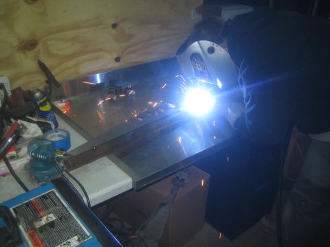 1990 Ford Bronco - Photograph of a fabricator MIG welding a steel plate on a shop workbench, not a technical document.