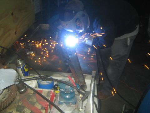 1990 Ford Bronco - Photograph of a person welding steel parts on a workbench amid a shower of sparks, not a technical document.