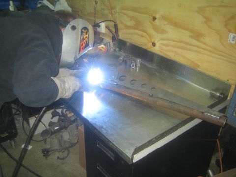 1990 Ford Bronco - Photograph of a fabricator welding a frame member with lightening holes on a shop bench, not a document.