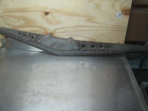 1990 Ford Bronco - Photograph of a fabricated FTF steel frame member with lightening holes leaning against a bench, not a document.